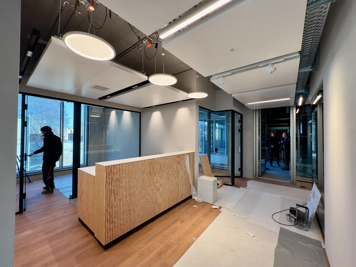 Man sieht einen Empfangstresen in der Mitte des Raumes. Der Boden ist an gewissen Stellen noch mit Bauflies abgedeckt. Von der Decke hängen drei grosse, runde Tellerlampen.